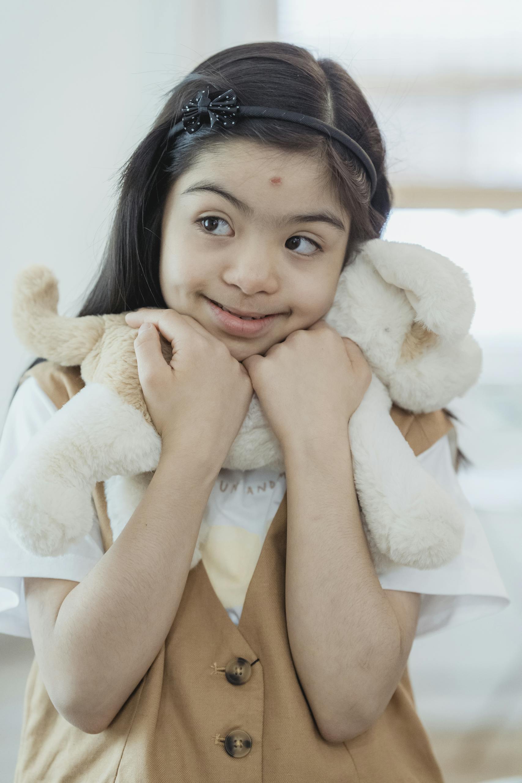 A young girl with Down syndrome warmly embraces a plush toy indoors, radiating joy and innocence.